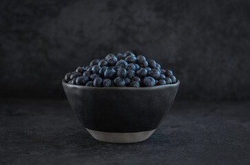 macro photo of fresh blueberry berries lying in a black ceramic bowl on a dark textured background