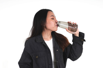 Asian young woman with long hair wearing black denim jacket drinking water from reusable gray water bottle container isolated on horizontal white background.