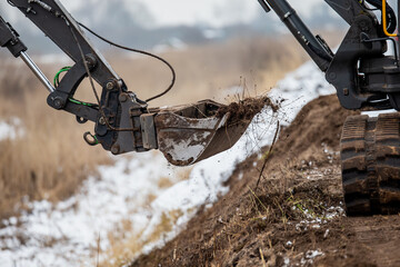Mini excavator leveling earth moving project works with dirt and snow mixing together in bucket....