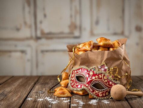 festive purim celebration essentials: traditional hamantaschen pastries, ornate mask, and grogger noisemaker on rustic wooden surface
