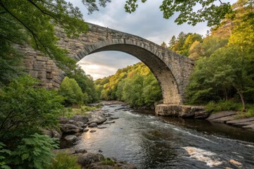 Fototapeta premium Stone arch bridge spanning the river with water flowing beneath and surrounding foliage, natural scenery, stone bridge