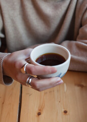 Young caucasian freelancer woman hold white cup with black filter coffee. Barista on cafeteria giving mug to customer top view. alternative brewing of specialty coffee, v60. background light wood