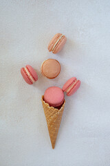 French rose macarons on light background in ice cream waffle cones, perfect for st Valentine's day and mother's day, Flat lay, with green leaves and flowers 