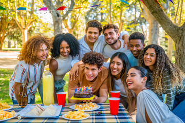 Young man blowing candles celebrating birthday with friends at park