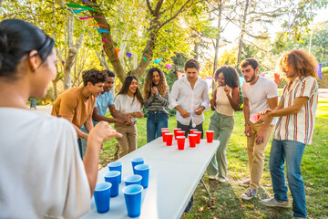 Happy young people playing beer pong under sun at park