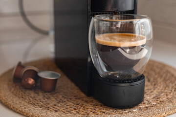 Coffee brewing in a modern espresso machine with a glass cup on a woven mat