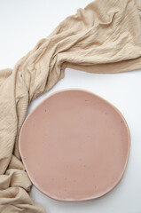 Empty ceramic plate with pastel beige fabric on white background. Mock up romantic tableware composition. Elegant minimalist layout concept for wedding invitation, dating or spa.