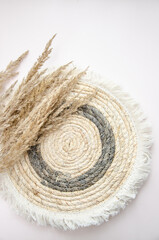A round woven placemat, and dry spikelets on a light beige background.dry spikelets. Mock up. Concept of home comfort and interior elements.