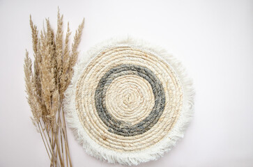 A round woven placemat, and dry spikelets on a light beige background.dry spikelets. Mock up. Concept of home comfort and interior elements.