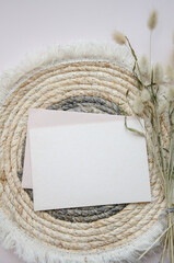 A round woven placemat, blank card and dry fluffy spikelets on a light beige background. Mock up. Concept of home comfort and interior elements. Restaurant promo. Buisness card.
