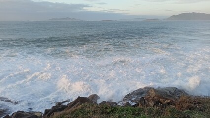 Stunning coastal scene featuring powerful ocean waves crashing against rugged rocks under a serene sky, with distant islands on the horizon