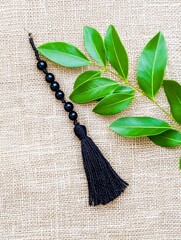 Black Beaded Cord with Tassel on Burlap - Elegance, simplicity, spirituality, nature, adornment.  A black beaded cord with a tassel rests on burlap next to green leaves.