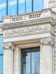 Fototapeta premium Elegant Architectural Stonework Detail - Close-up view of ornate stone columns and detailing above a modern glass window, showcasing classic architectural elements.