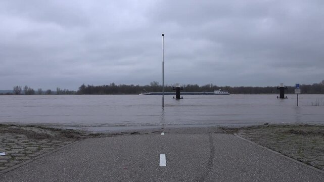 Abstract shot of flooded road and cargo boats sailing on the Rhine river in Tolkamer, high water levels in Europe
