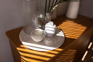 Ceramic tray on a wooden chest of drawers in the bedroom. Handmade scented candles, a carafe of water and a vase with a green leaf.