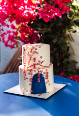 A cute white two-tiered delicious cake on a blue table. The sweetness is decorated with pink flowers