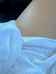Sun-kissed woman's leg draped in white linen fabric close-up