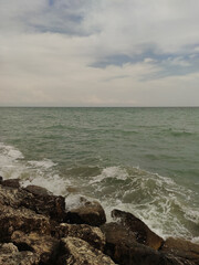 Gentle waves washing rocky shore under overcast sky, depicting seascape along adriatic coastline in bibione, italy during summer, perfect for backgrounds, graphic design, and interior decoration