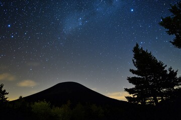 Naklejka premium Starry Night Sky Over Mountain Silhouette with Twinkling Stars and Dense Forest in Foreground: Awe-Inspiring Grandeur and Tranquility of Nature