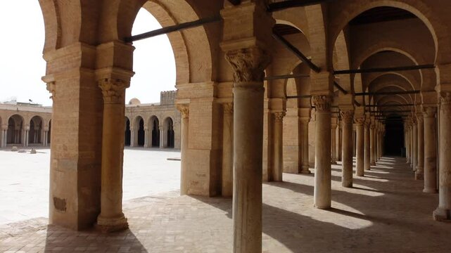 Walking through arches inside the courtyard of the Great Mosque of Kairouan, historic Islamic architecture and landmark in Tunisia
