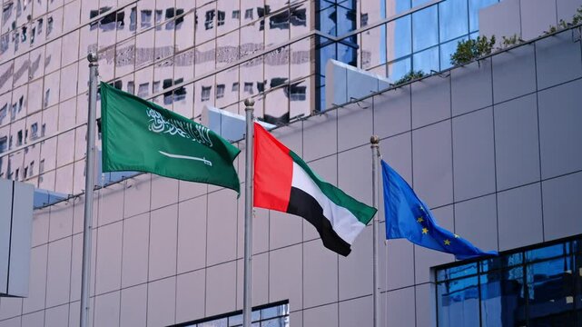 Flags of Saudi Arabia, United Arab Emirates, European Union waving against a backdrop of modern buildings. A powerful symbol of international cooperation and urban progress