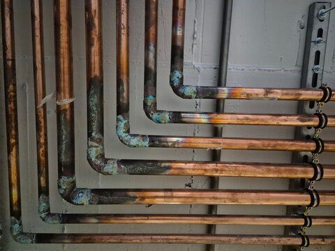 Multiple copper pipes running horizontally along a wall, revealing signs of oxidation and welds, create a visually striking textured pattern in an industrial setting
