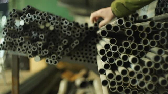 In production, the metal is laid out according to size and shape. A man's hand picks up one of the pipes for work. High quality 4k footage