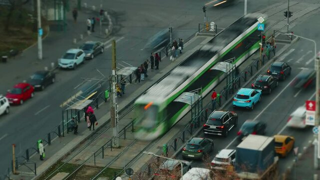 Green tram pausing for passenger exchange at bustling Bucharest intersection, capturing urban transportation dynamics during evening rush hour commute
