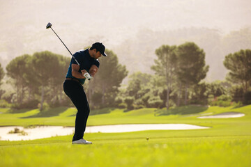 Golfer swinging at a golf ball on a lush golf resort, demonstrating perfect form and focus on a...