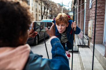 Kid making funny face while friend takes a photo on smartphone outdoors