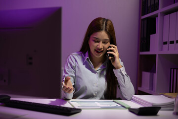 A woman is talking on her cell phone while sitting at a desk. She is wearing a striped shirt and...