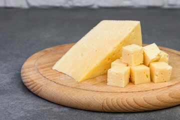 Sliced cheese on wooden board on gray background.