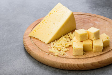 Sliced cheese on wooden board on gray background.