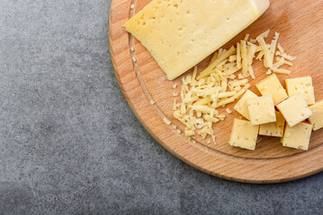 Sliced cheese on wooden board on gray background.