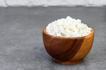 Cottage cheese in wooden bowl on gray background.