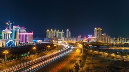 Obraz premium Vibrant night highway with light trails stretching towards the illuminated city skyline. The mesmerizing view of a busy thoroughfare at night, where the streaks of light from vehicles create a beautif
