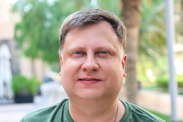 Fototapeta premium Portrait of a man in a green summer t-shirt on a hot day under the shade of city trees.