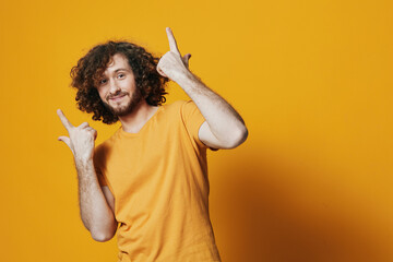 Young man with curly hair in a cheerful yellow shirt poses against a bright yellow background,...