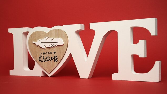 Love word sculpture. Heart wood insert. Feather shape detail. Red romantic background.
