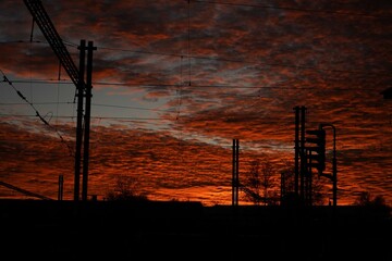 Railway power lines. Dramatic sunset sky. Industrial silhouette view. Orange cloud texture.
