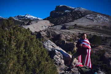 Person wrapped in flag enjoying scenic mountain view with clear blue sky