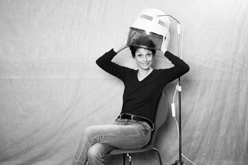 schwarz-weiß Portrait einer Frau mit kurzen Haaren, die unter einer Retro Trockenhaube sitzt und...