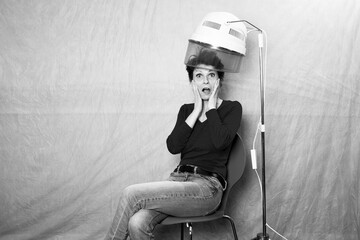 schwarz-weiß Portrait einer Frau mit kurzen Haaren, die unter einer Retro Trockenhaube sitzt und...