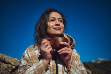 Woman outdoors holding a wooden cup, enjoying the fresh air on a sunny day