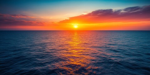 Fototapeta premium Vibrant sunset over a calm ocean. Orange, yellow, and purple hues paint the sky, reflecting on the dark blue water. Peaceful and serene atmosphere