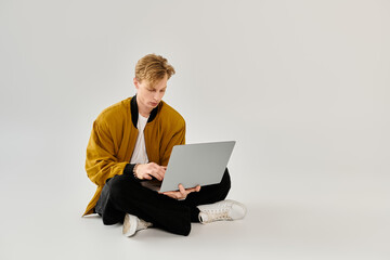 Young handsome man working intently on a laptop while sitting comfortably on the floor