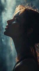 Profile of a young woman with reddish brown hair, illuminated by dramatic lighting against a smoky, dark background. Her expression is pensive