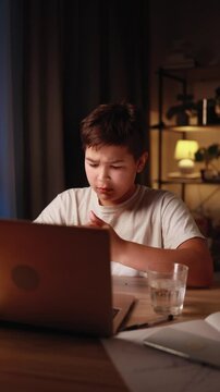 Teen boy sitting at desk stretching neck and feeling pain after long screen time or online studying at home Child with beck discomfort after hours of remote learning
