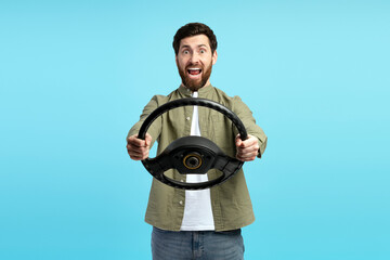 Surprised young man posing with auto steering wheel, isolated on blue background
