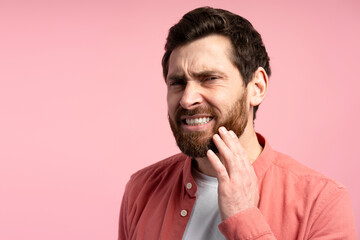 Young bearded man touching cheek and wincing in pain feeling terrible tooth ache